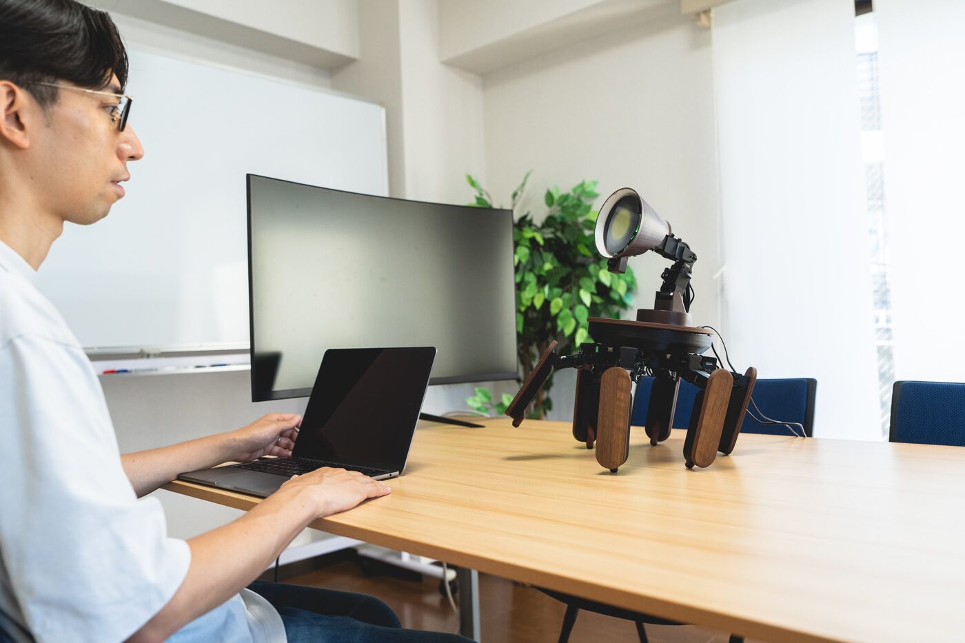 Palmimo standing on a desk beside a developer at a laptop, its round face display lit yellow
